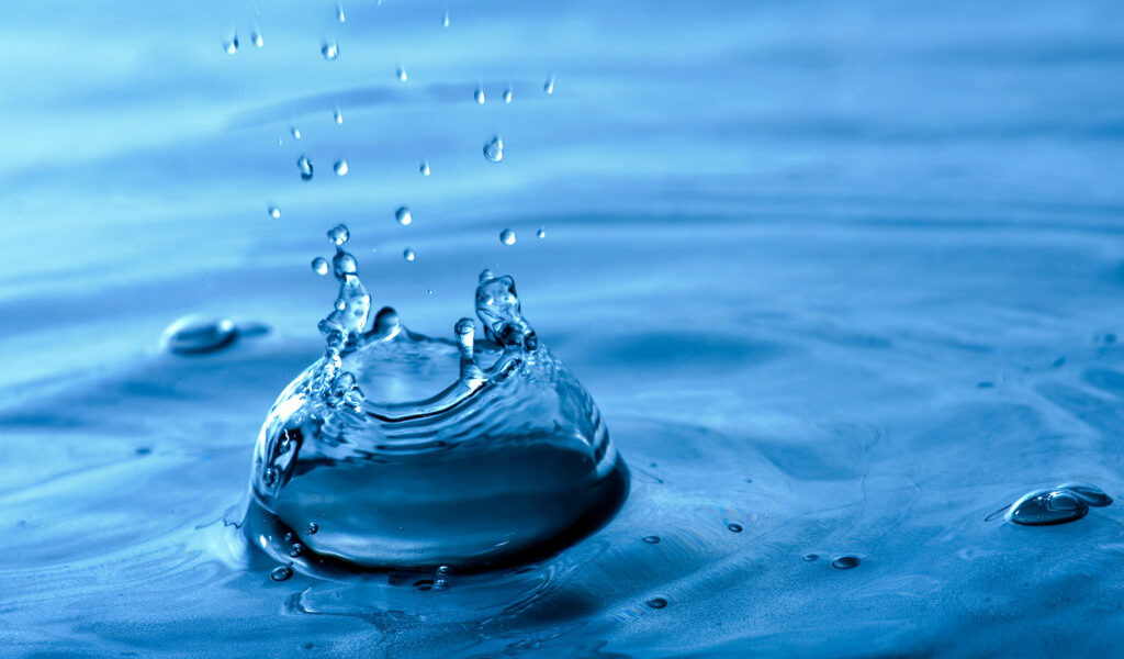 A blue water background texture and splash with droplets forming a crown shape. Shallow depth of field.